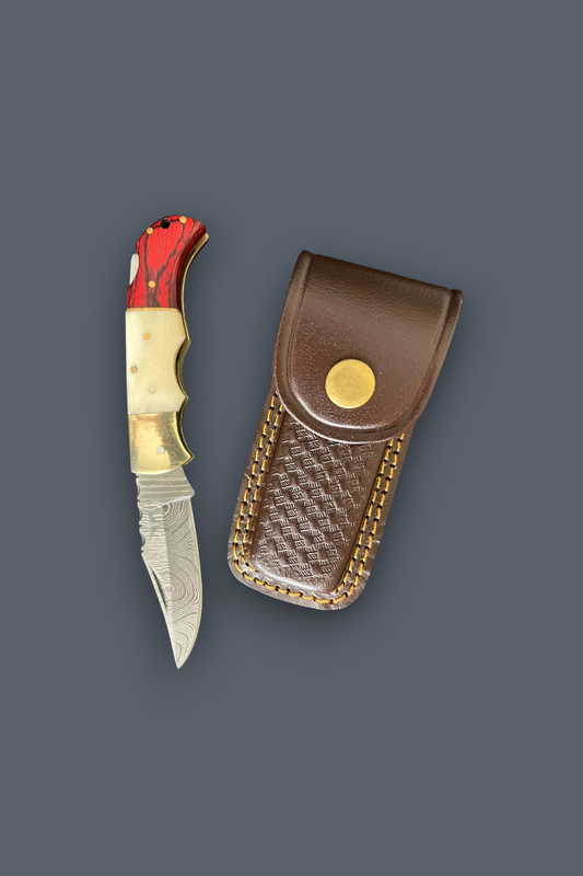 A folding pocket knife with a silver patterned blade, red and cream handle, and a brown leather sheath with gold-toned trim, displayed on a solid dark gray background.