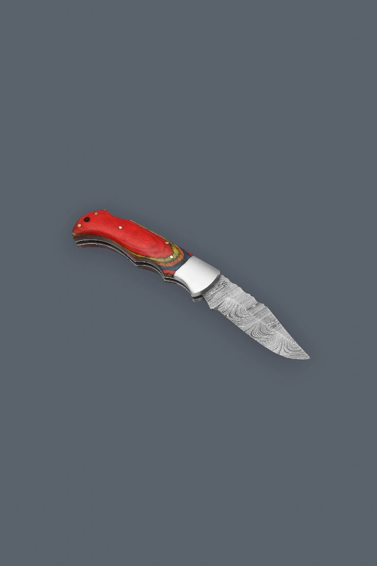 Angled flat lay of the fully open Olde Townie Damascus folding knife showcasing the steel bolster and multicolor wood handle