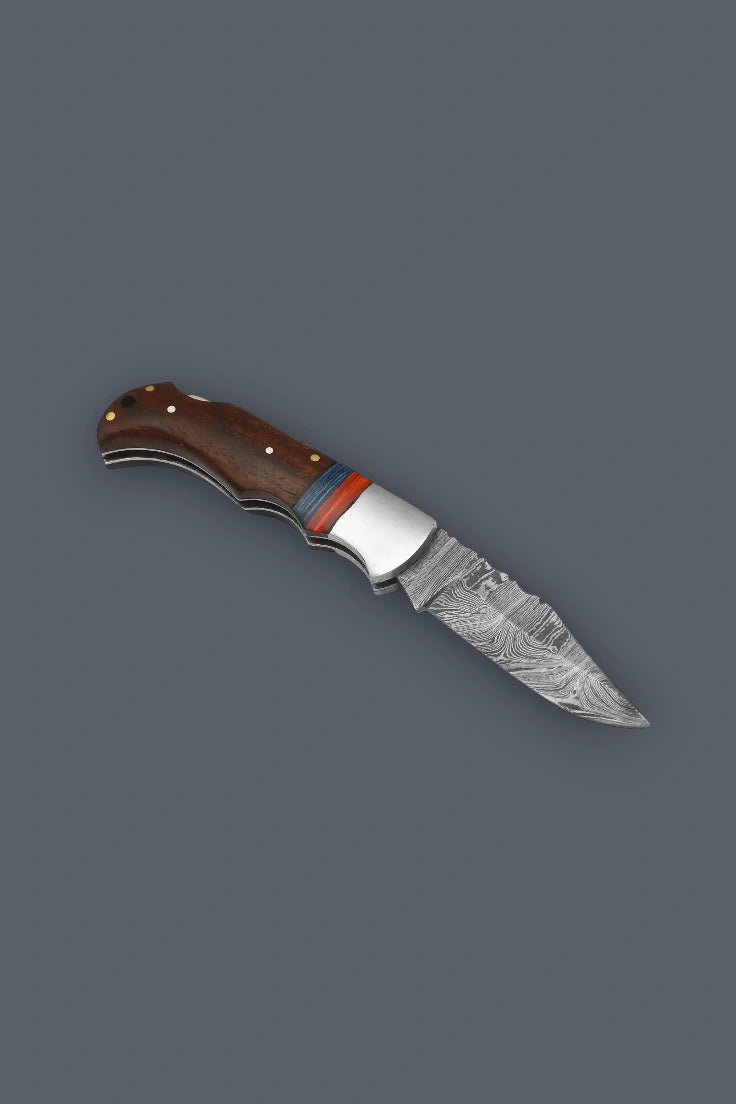 Angled flat lay of the fully open The Gentry Knife showcasing the distinctive Damascus blade, smooth silver bolster, and custom wood handle.