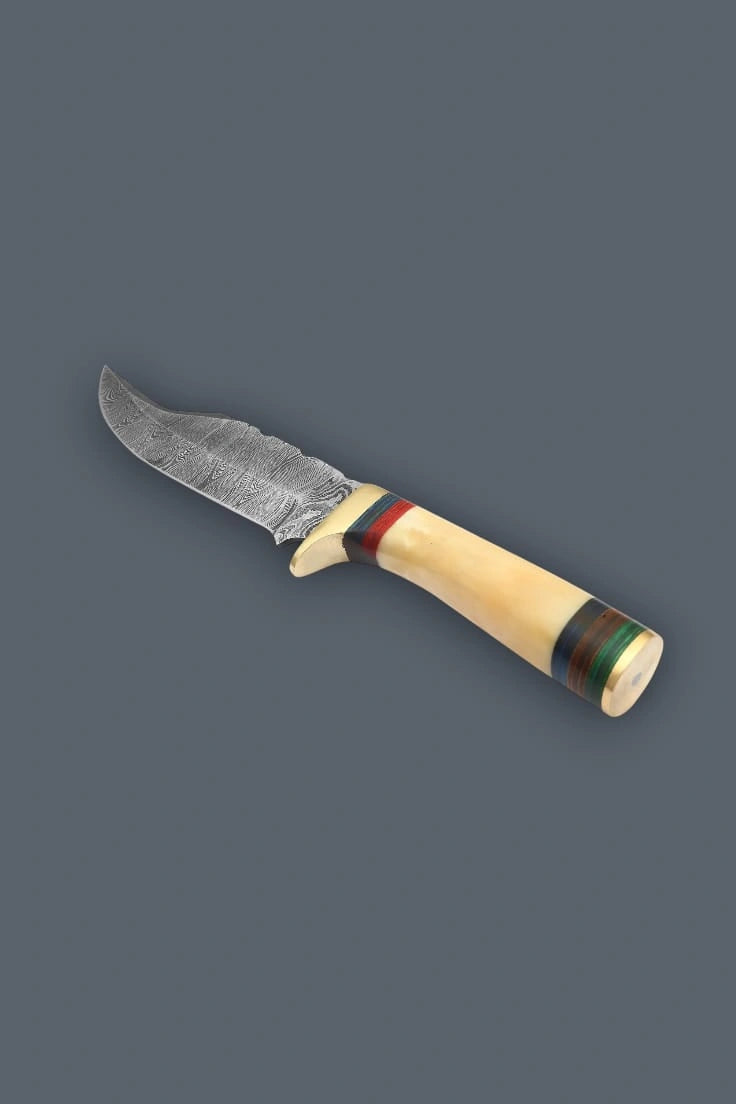 Upward diagonal flat lay of the Damascen Knives fixed blade hunting knife, showcasing the wavy Damascus steel pattern, brass crossguard, and banded bone handle.