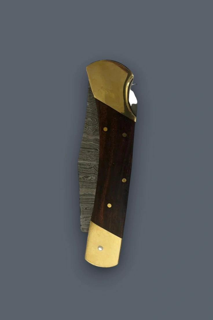 Vertical flat lay of the closed Old World Edge Damascus knife with wood handle and brass bolsters.