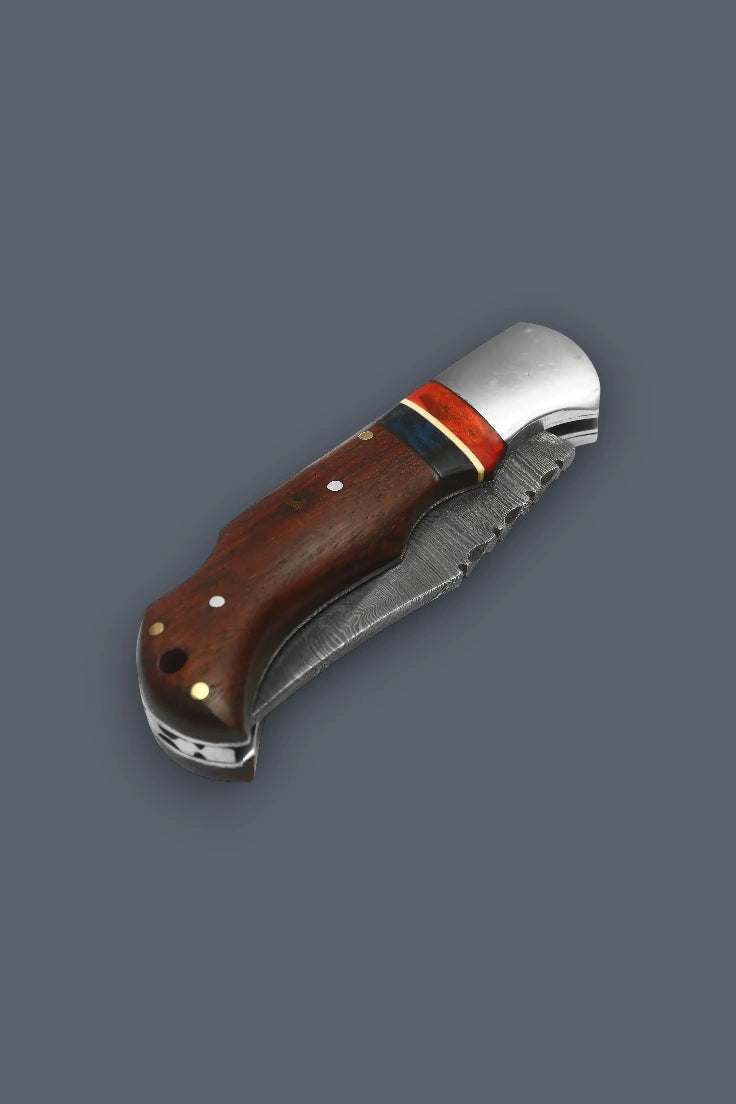 Diagonal close-up of the fully closed The Gentry Knife showcasing a smooth silver bolster, spine filework, and a custom wood handle.