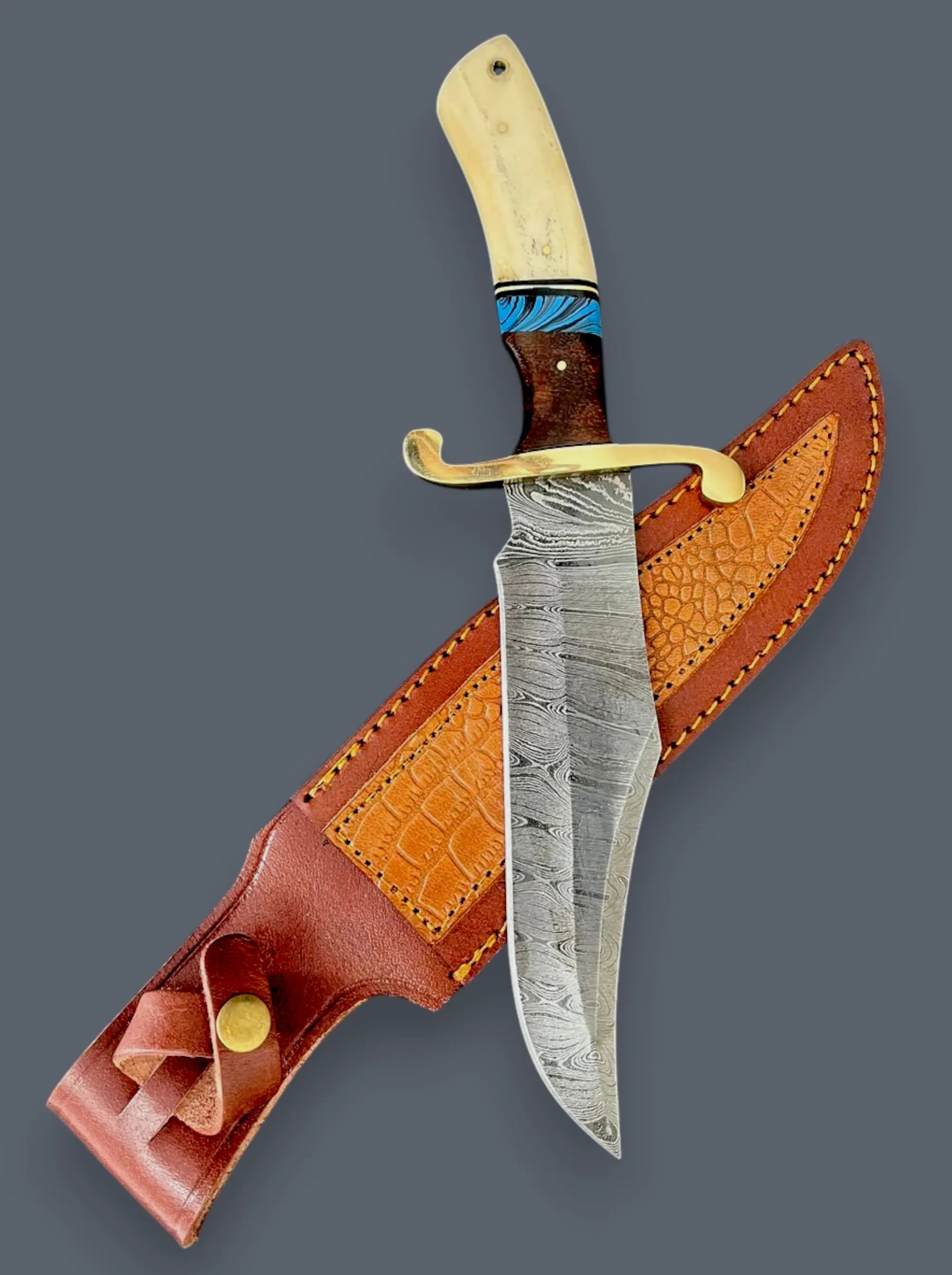 A custom fixed-blade knife with a patterned steel blade, a dark wood handle with turquoise inlay, and a brass guard, shown alongside its brown leather sheath on a solid dark gray background.