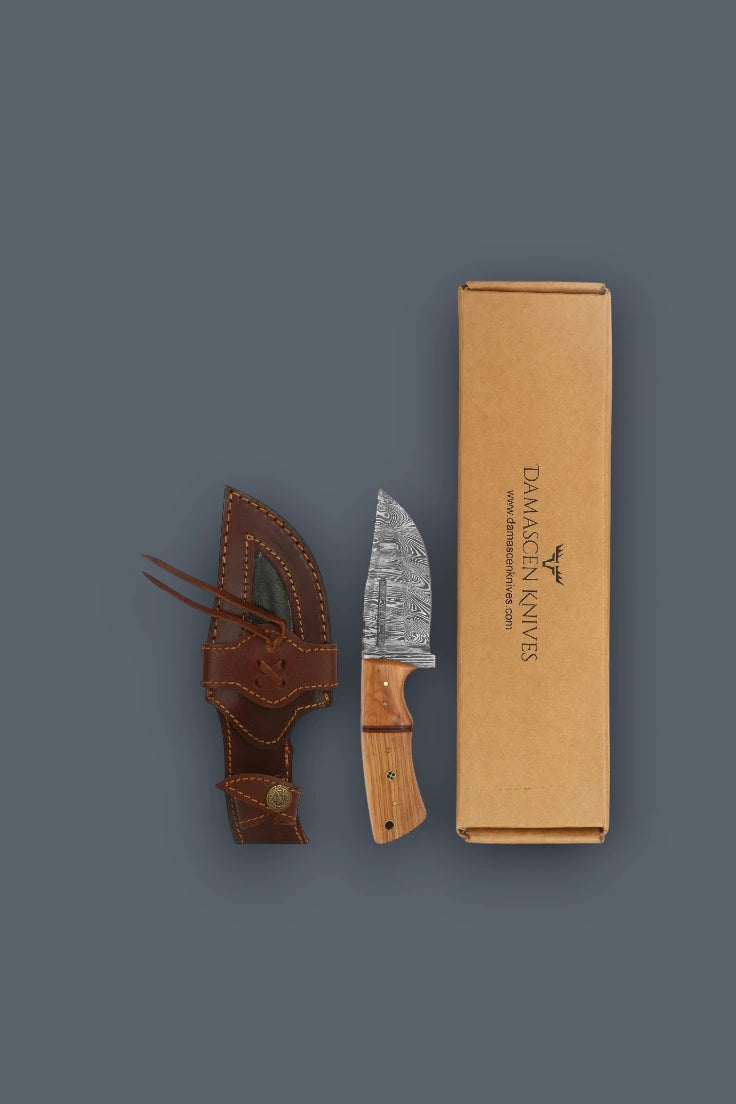 Vertical flat lay of the Damascus fixed blade hunting knife with wooden handle, cowhide leather sheath, and branded gift box.