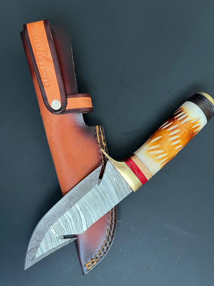Full-tang Damascus steel fixed blade knife resting beside stitched cowhide leather sheath.