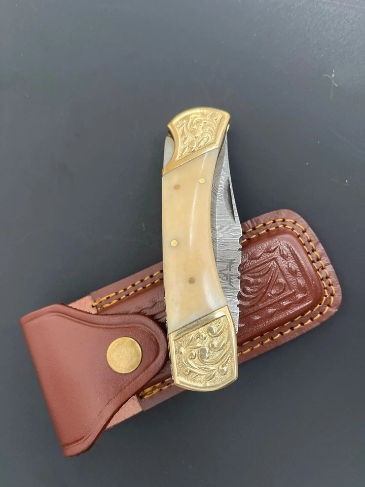 Partially open Damascus steel folding knife showing patterned 5-inch blade and bone handle.