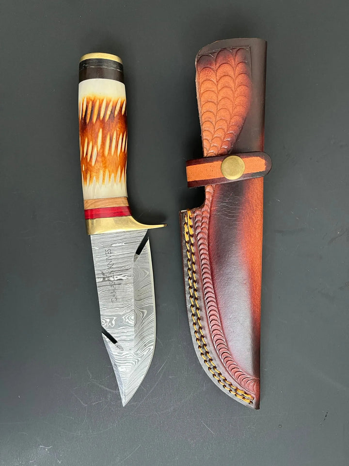 Close-up of Damascus steel blade and horn handle with orange-brown burned wood accent.