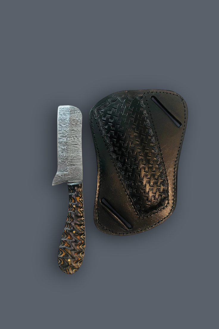 A small damascus razor blade knife with a textured silver blade and a patterned brown handle, shown next to a dark brown woven leather sheath on a solid dark gray background.