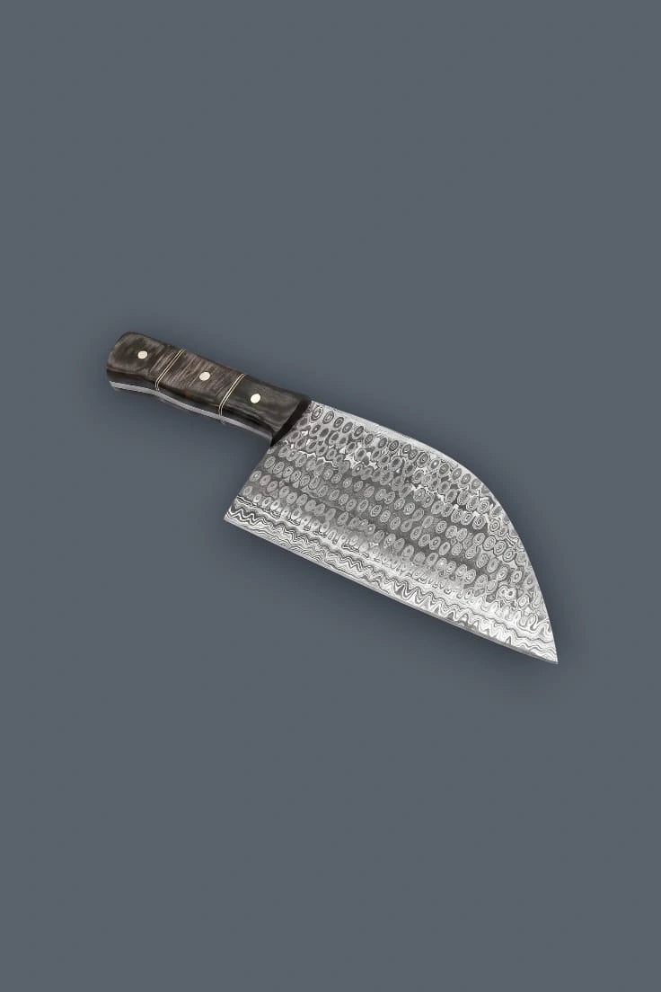 Downward diagonal flat lay of the Damascus meat cleaver, showcasing the distinct circular hammered pattern on the broad blade and the triple-riveted Pakkawood handle.