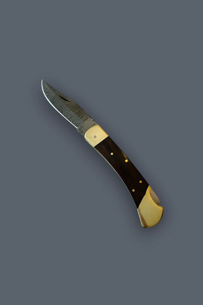 Diagonal flat lay of the fully open Old World Edge Damascus knife, highlighting the curved profile, wood handle, and brass bolsters.