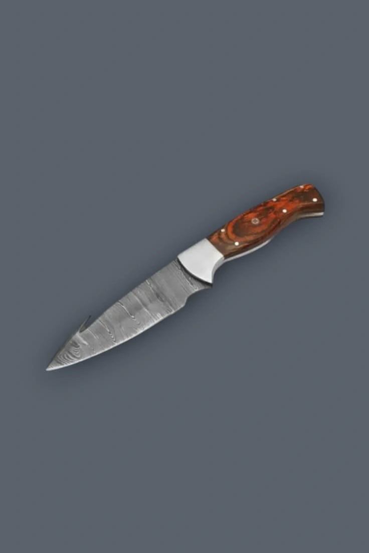 Downward diagonal flat lay of a fixed blade Damascus hunting knife, emphasizing the polished silver bolster, spine gut hook, and contoured wood handle.