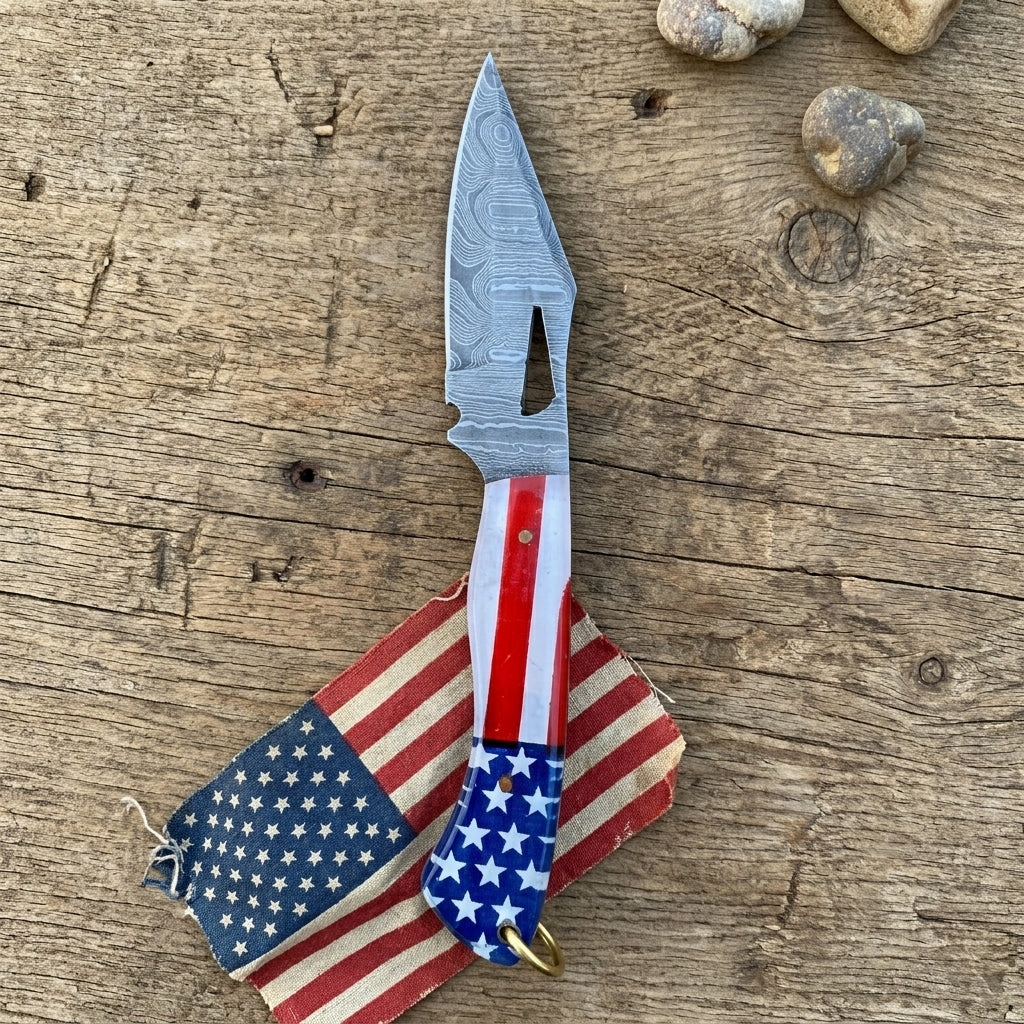 A fixed blade knife with a patterned steel blade and an American flag-themed handle, resting on a small matching American flag pouch over a rustic wooden surface.