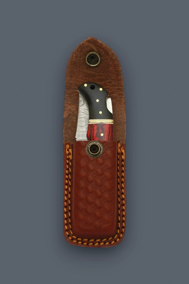 Folded Pioneer Pocket Damascus folding knife displaying its multicolor wood handle inside an open basketweave sheath.