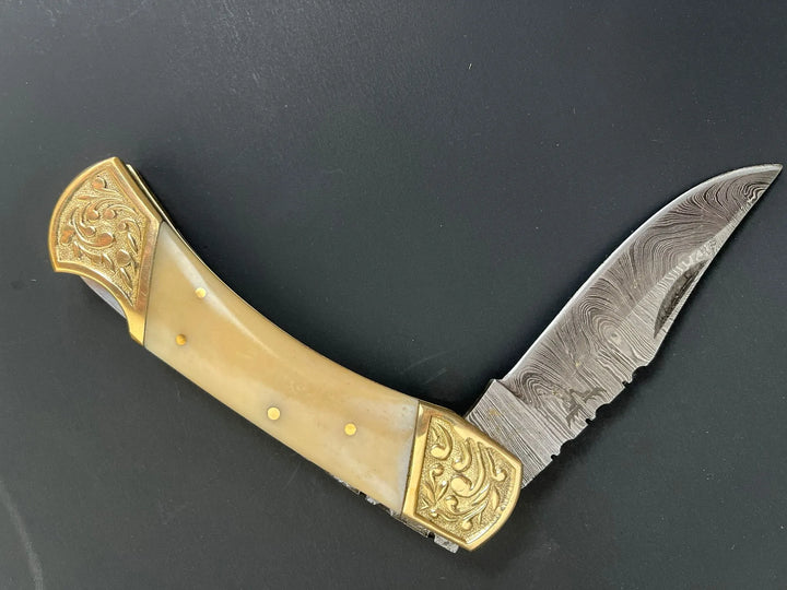 Closed Damascus pocket knife with bone handle beside brown leather sheath.