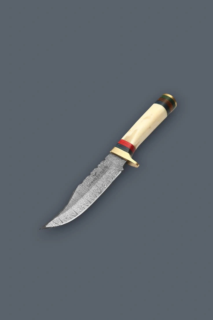 Downward diagonal flat lay of the Damascen Knives fixed blade, highlighting the sharp trailing point tip, intricate Damascus steel pattern, and banded bone handle.