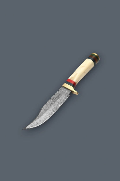 Downward diagonal flat lay of the Damascen Knives fixed blade, highlighting the sharp trailing point tip, intricate Damascus steel pattern, and banded bone handle.