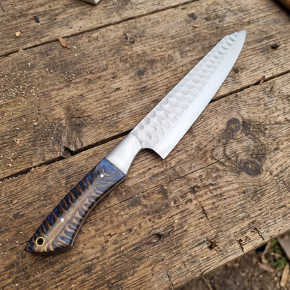 A kitchen knife with a hammered silver blade and a blue patterned handle, resting diagonally on a rustic wooden plank surface.