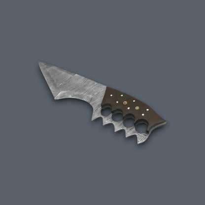 A miniature tactical knife with a textured silver-gray blade and a dark brown handle featuring finger grooves and brass pins, shown on a solid dark gray background.