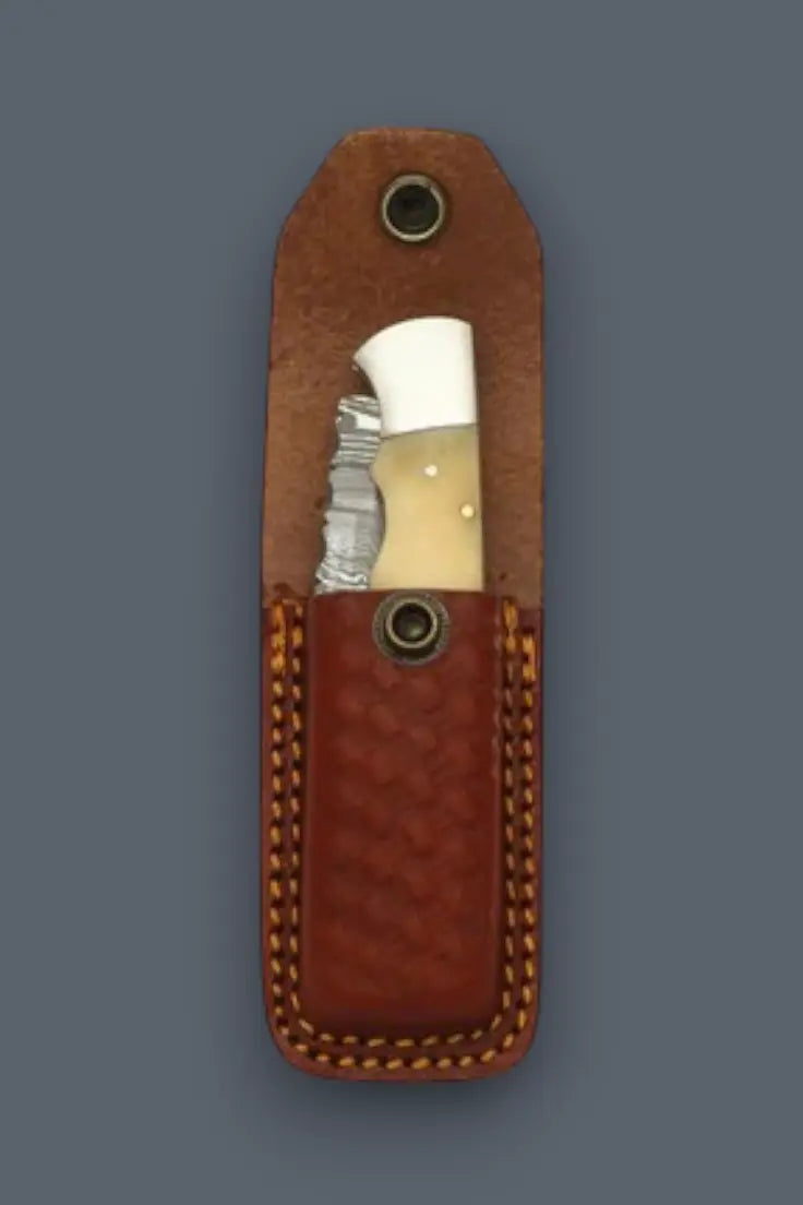 Bone handle lockback Damascus folding knife tucked into a heavy-duty leather sheath.