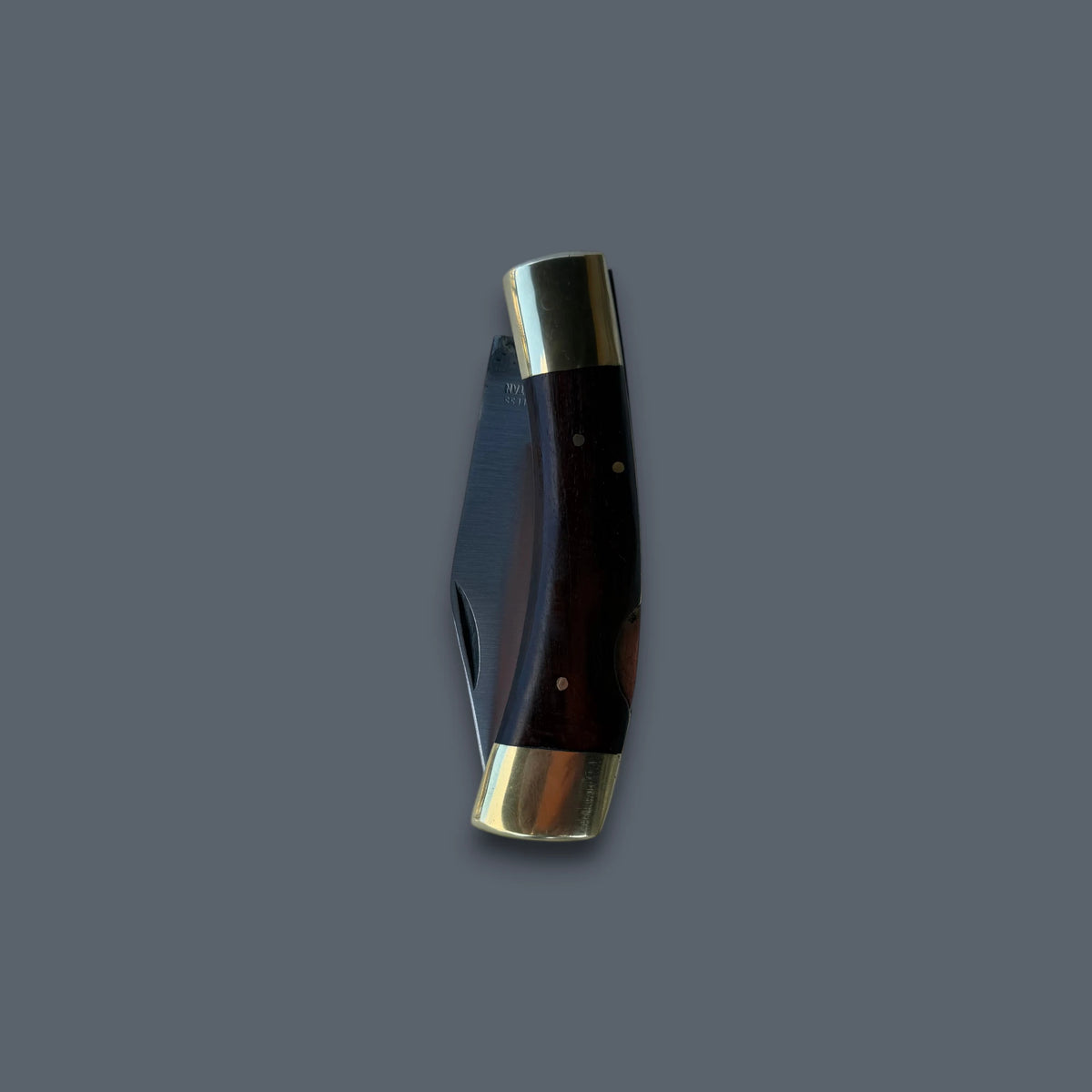 A folding pocket knife with a dark brown wooden handle and polished brass bolsters, shown partially open against a solid dark gray background.