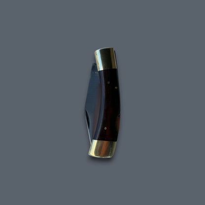 A folding pocket knife with a dark brown wooden handle and polished brass bolsters, shown partially open against a solid dark gray background.