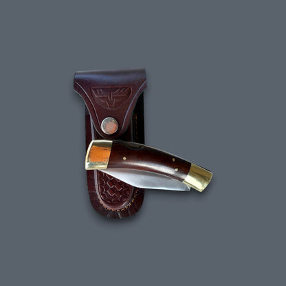 A folding pocket knife with a dark brown wooden handle and brass bolsters, shown partially deployed next to its matching dark brown leather sheath on a solid dark gray background.