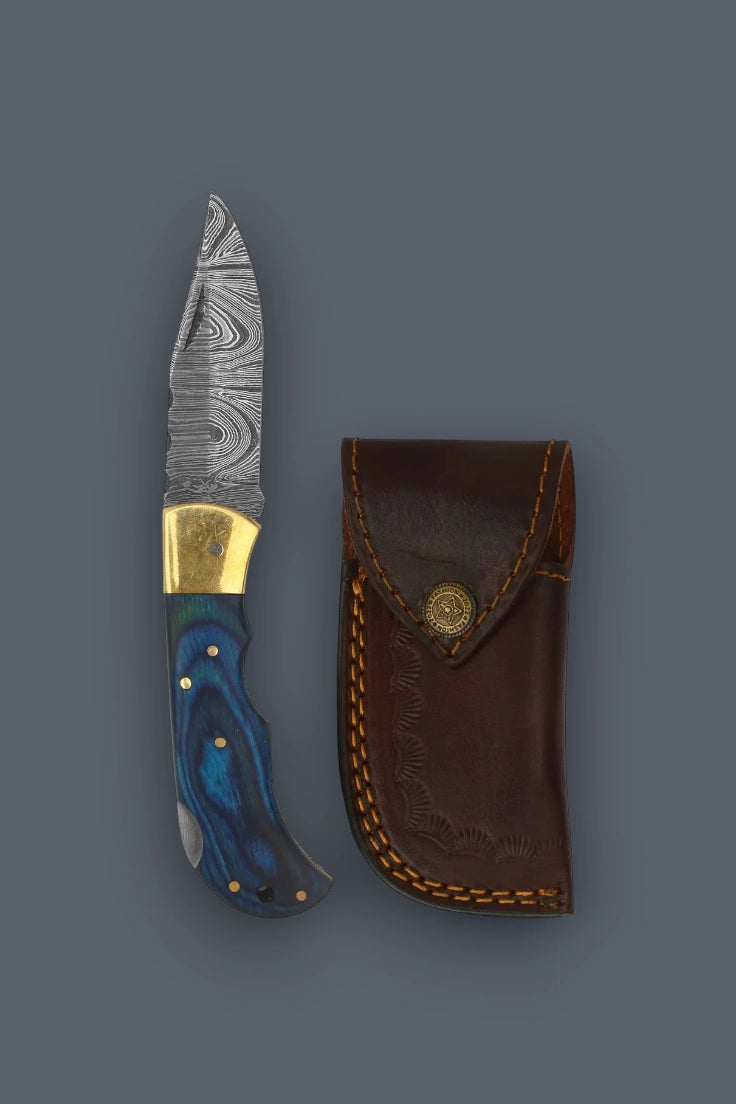 Flat lay of the partially open The Vanguard Damascus folding knife at a 90-degree angle, showcasing the blue pakkawood handle and brass bolsters.