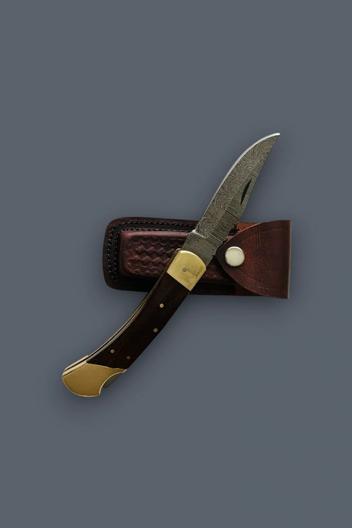 Partially open Old World Edge Damascus knife positioned next to its brown leather sheath.