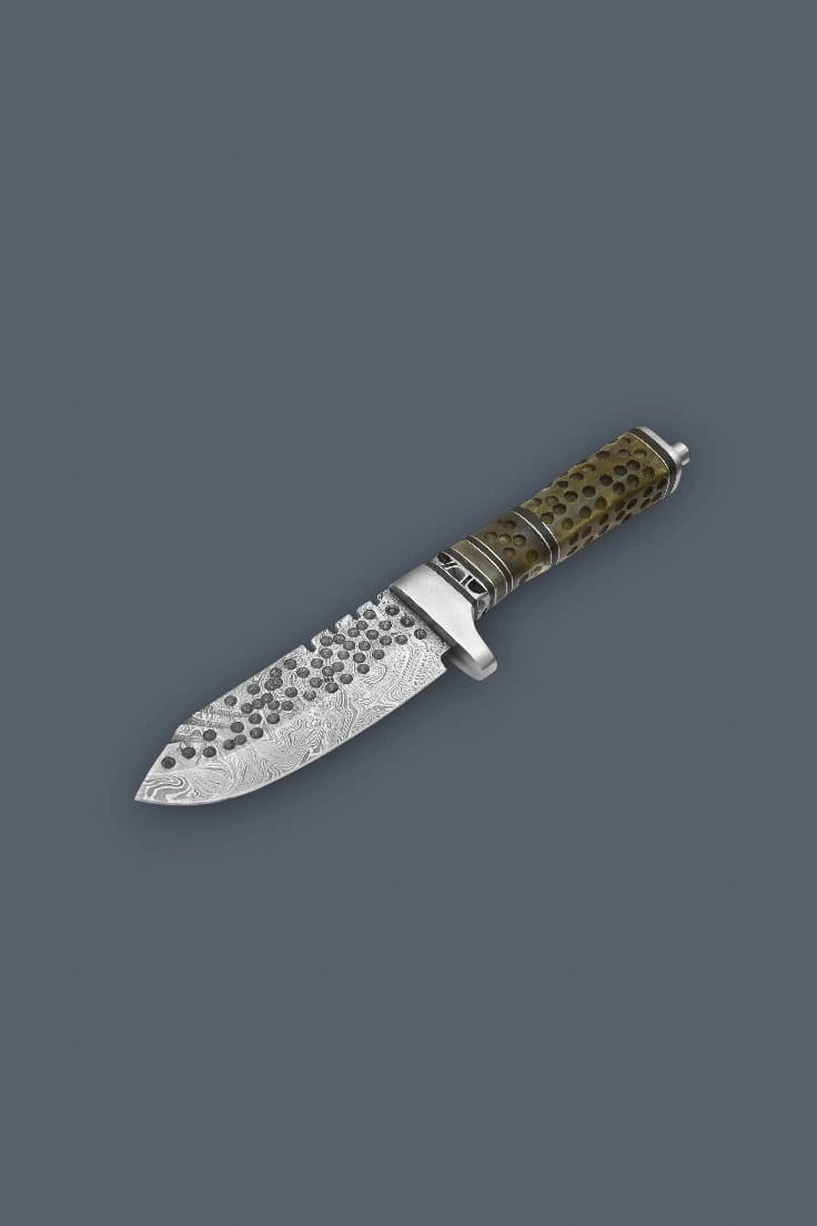 Downward diagonal flat lay of the Damascen Knives fixed blade, highlighting the prominent metal pommel, protective crossguard, and wavy Damascus steel pattern.