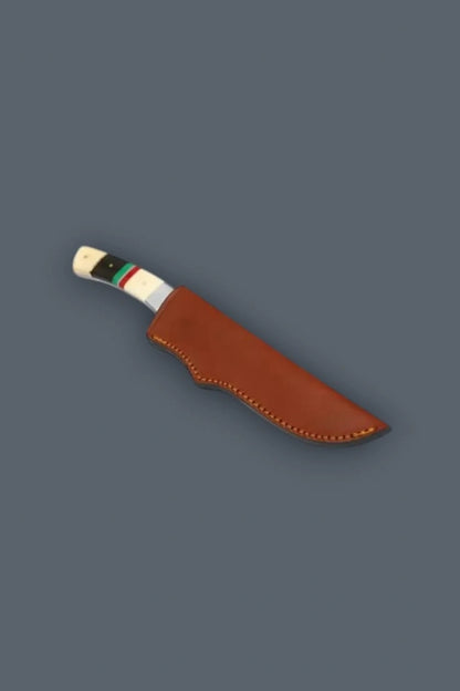 Diagonal flat lay of the stainless steel fixed blade hunting knife secured inside its genuine brown stitched leather sheath, exposing the custom banded bone handle.