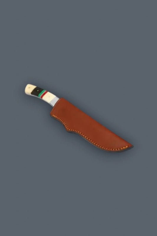 Diagonal flat lay of the stainless steel fixed blade hunting knife secured inside its genuine brown stitched leather sheath, exposing the custom banded bone handle.