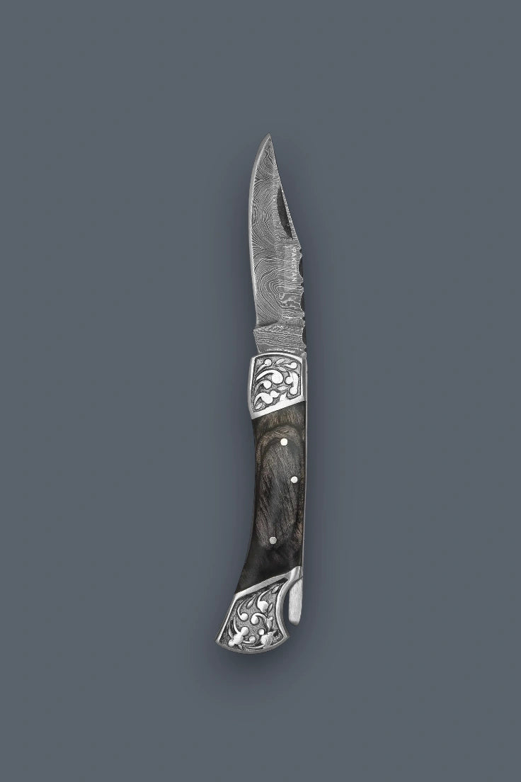 Diagonal flat lay of the fully open The Squire Damascus folding knife emphasizing the engraved silver bolsters and lockback mechanism.