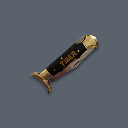 A folding pocket knife with a black handle and polished gold-toned metal accents, featuring the brand name 'TIGER' in gold on the handle, set against a solid dark gray background.